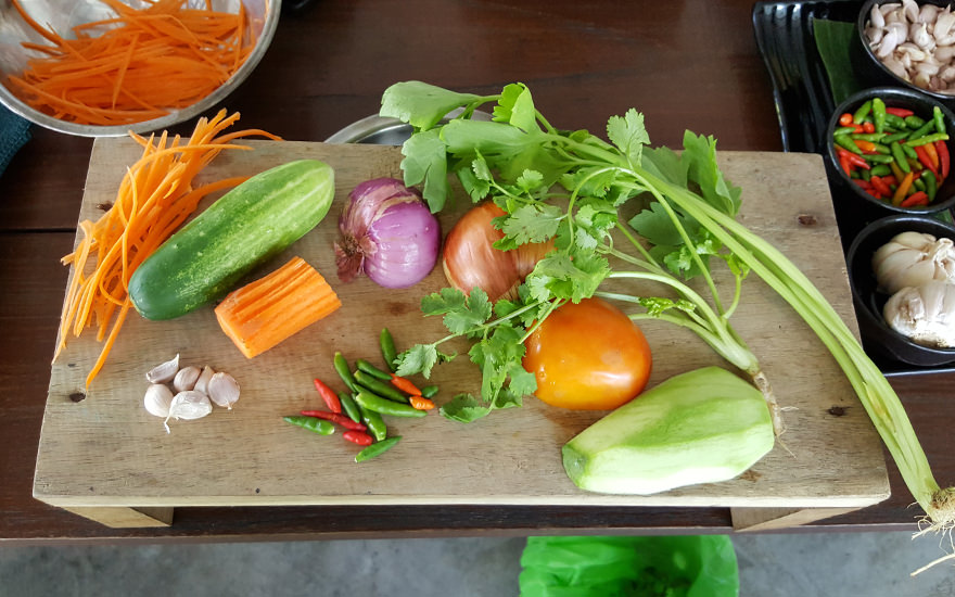Zutaten auf einem Holzbrett bei einem Thai-Kochkurs: Chilischoten, Koriander, Mango, Tomaten etc.
