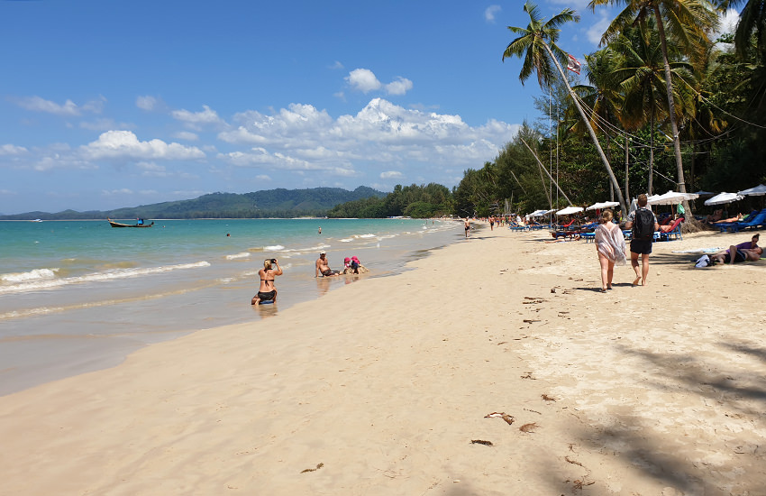 Coconut Beach in Khao Lak mit hellem Sand, türkisfarbenem Wasser, Spaziergängern und weißen Sonnenschirmen