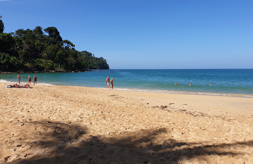 Sunset Beach in Khao Lak mit goldgelbem Sand und bewaldetem Hügel am Ende der Bucht
