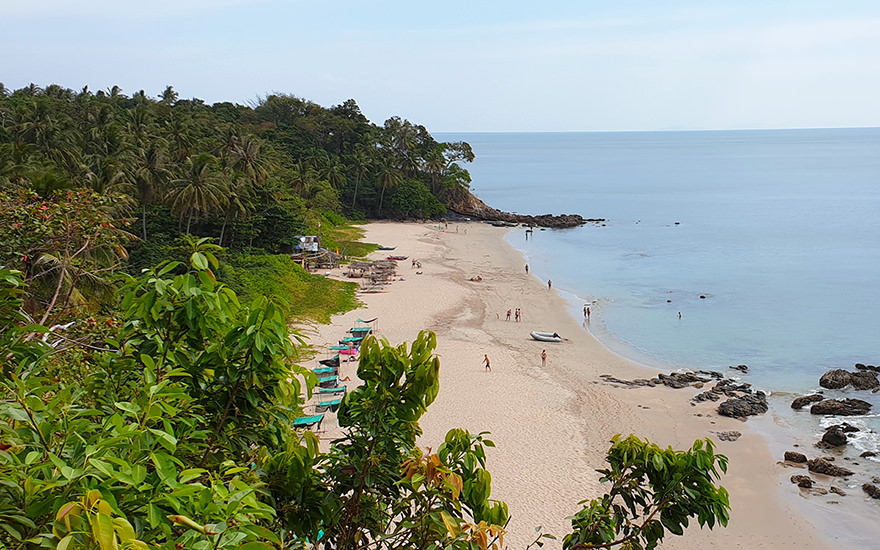 Blick von oben auf den Nui Beach auf Koh Lanta mit Palmen, vereinzelten Felsen und Menschen