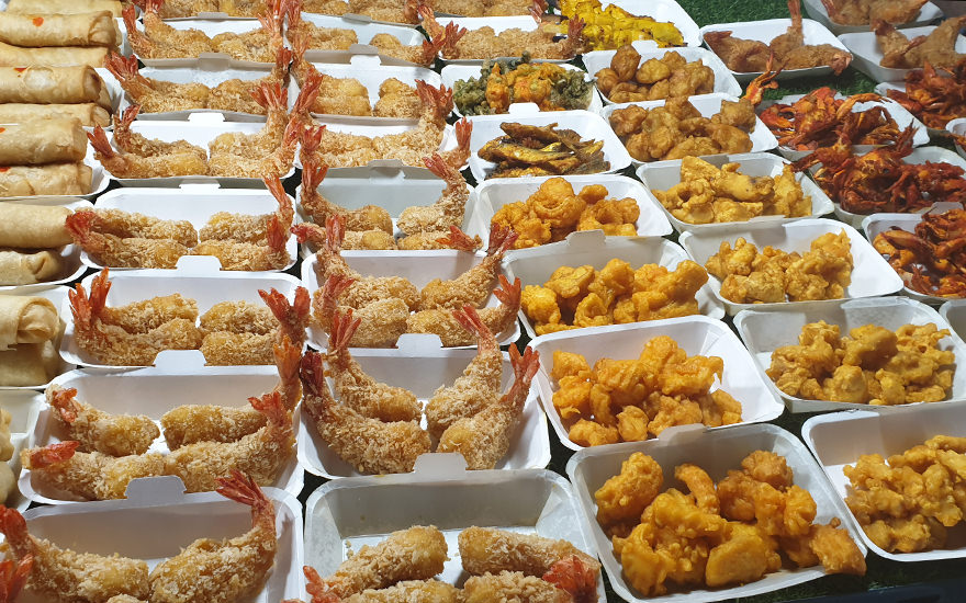 Styropor-Schälchen mit panierten frittierten Garnelen, Frühlingsrollen und Gemüse-Tempura