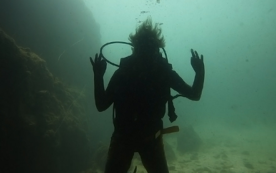 Konturen einer Taucherin im grünen Wasser nahe einer Felswand